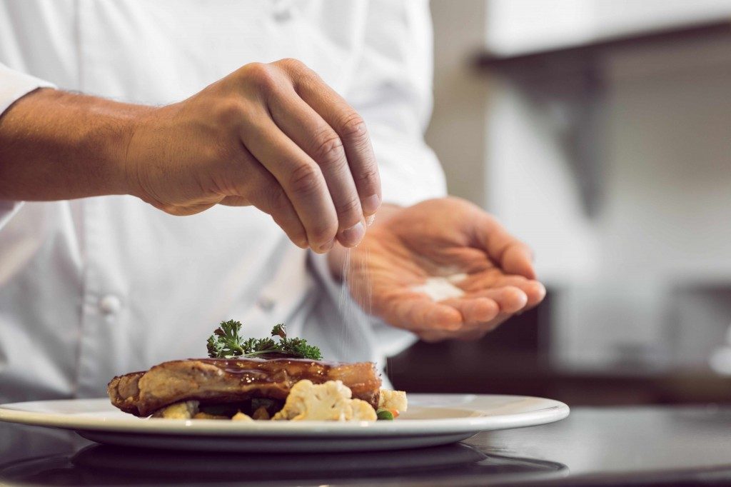 a man sprinkling salt on a meat dish in a restaurant