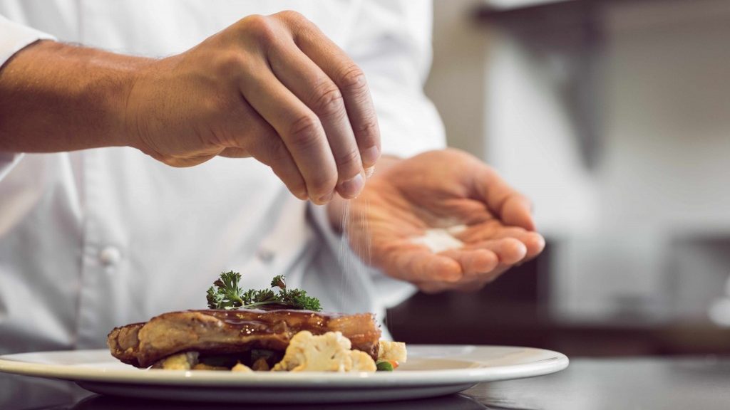 a man sprinkling salt on a meat dish in a restaurant