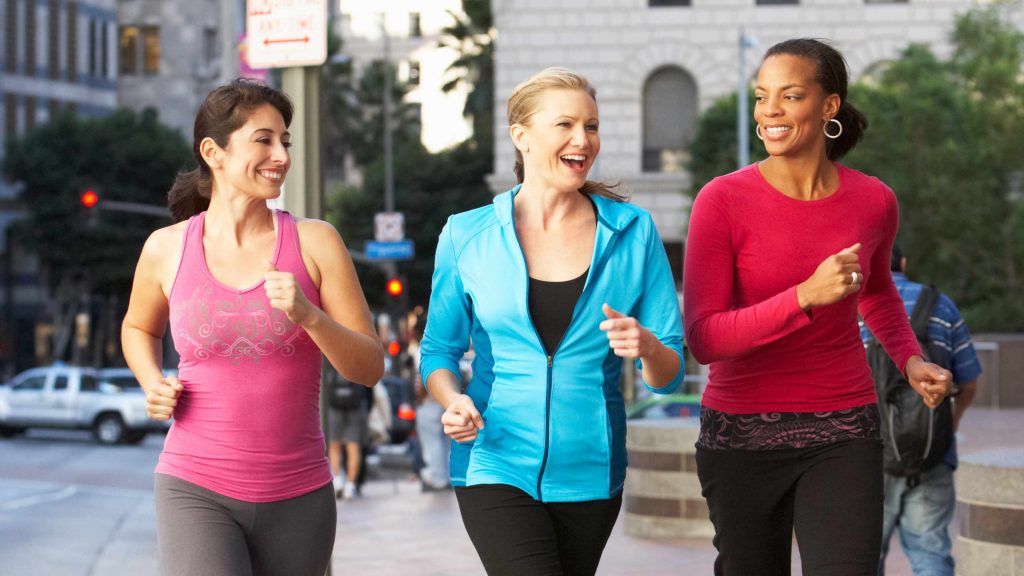 three smiling young women walking vigorously along a city sidewalk